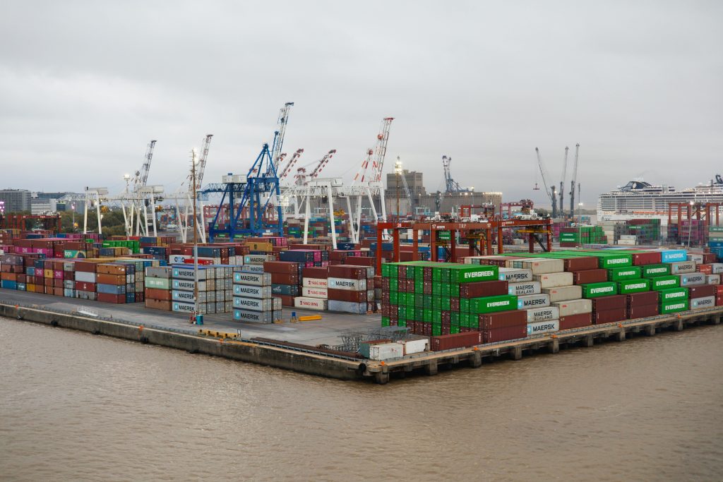 A bustling shipping port with stacked cargo containers and cranes under overcast skies.